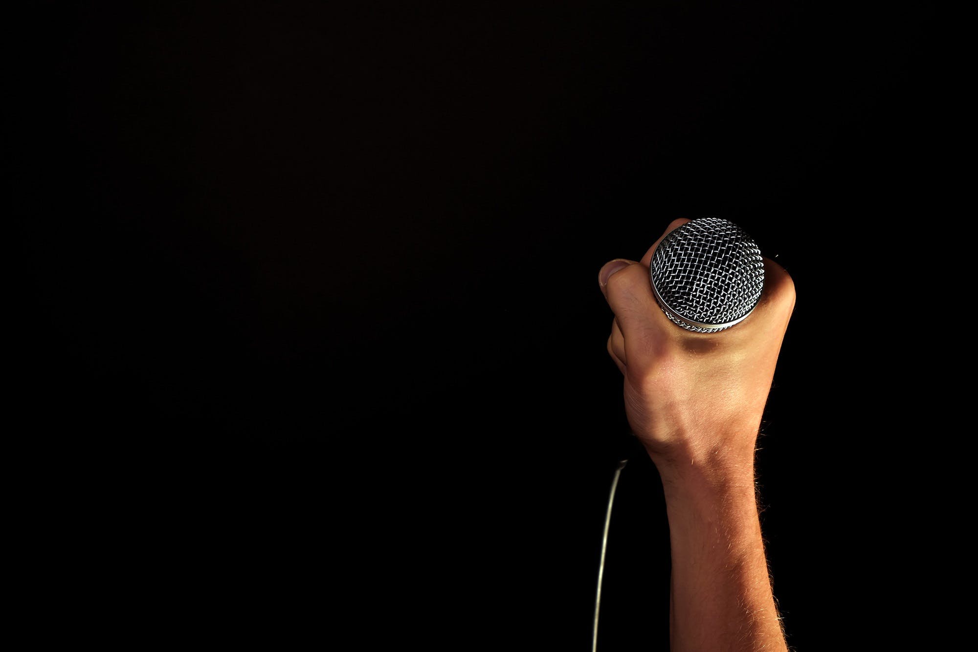 An image of a caucasian hand gripping a microphone against a black backdrop